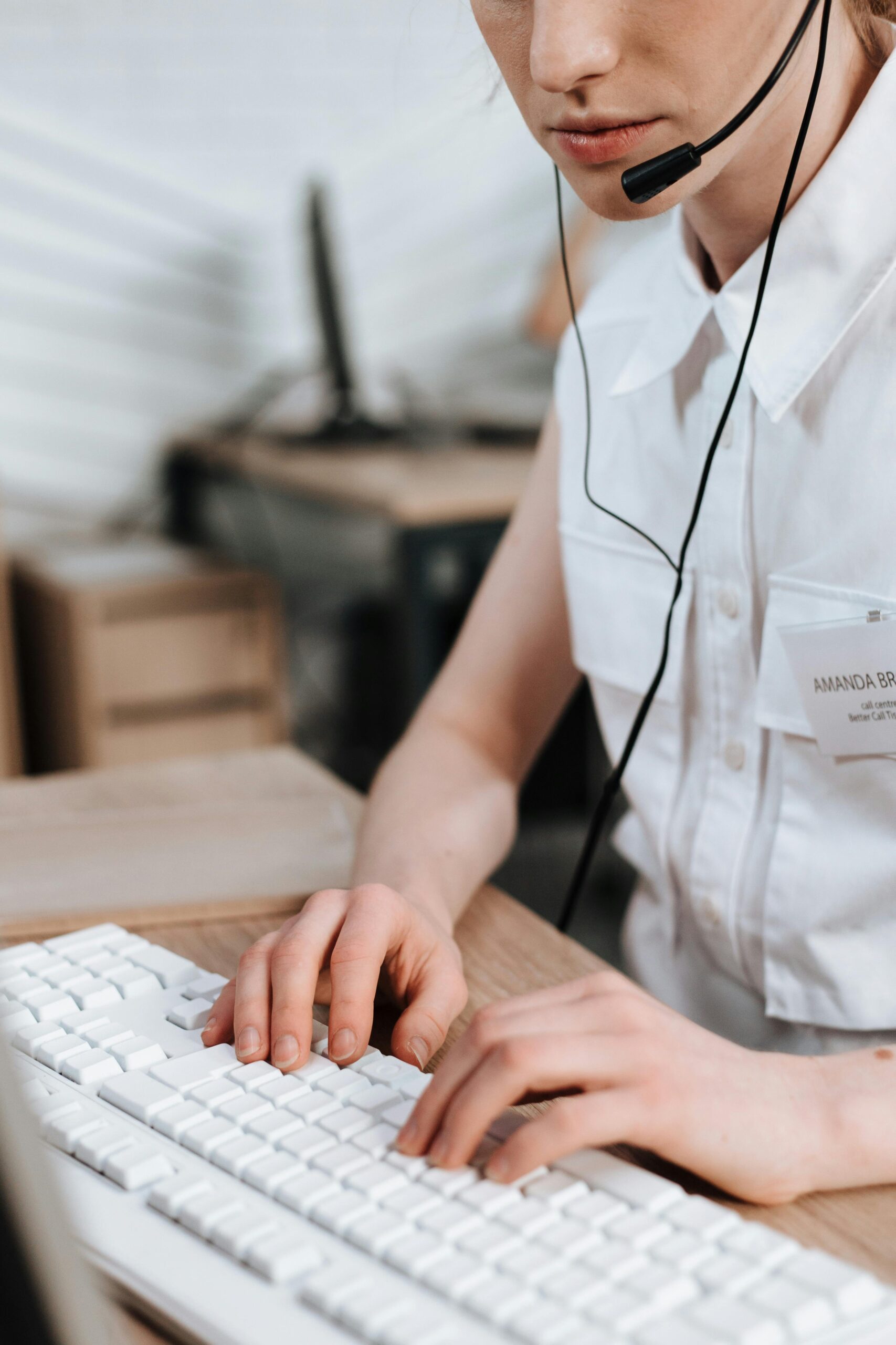 Close-up of a female call center agent typing on a keyboard, wearing a headset in an office setting.